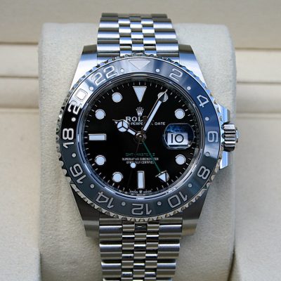 Rolex 126710GRNR | SD Watches Close-up of a stainless steel Rolex GMT-Master II watch with a black dial and wavy bezel on a beige cushion display.