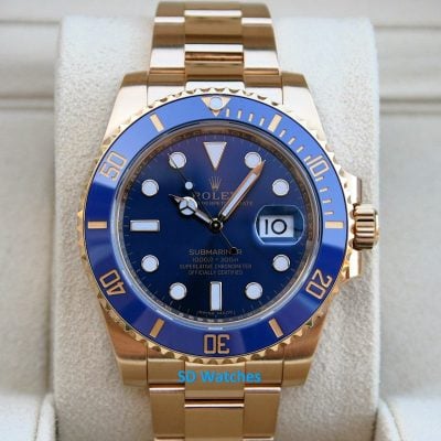 Gold Rolex Submariner watch with a blue bezel resting on a light display cushion.