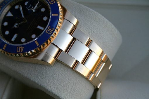 IMG_6481 | SD Watches Close-up of a two-tone wristwatch with a blue bezel, black dial, and gold-and-silver bracelet on a soft gray surface/glove edge.