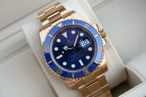 IMG_6490 | SD Watches Gold Rolex Submariner watch with a blue bezel and blue dial resting on a light-colored cushion, showing the date window at 3 o'clock and a gold bracelet
