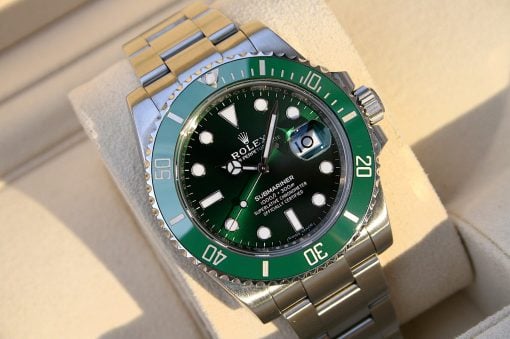 IMG_6558 | SD Watches Close-up of a Rolex Submariner watch with a green bezel and stainless steel bracelet on a beige surface, showing the date window magnifier.