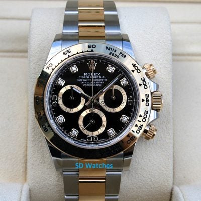 Two-tone Rolex Daytona watch with black dial, diamond hour markers, on a beige display cushion.
