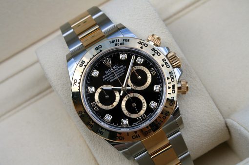 IMG_6688 | SD Watches Two-tone Rolex Cosmograph Daytona wristwatch with black dial and diamond hour markers resting on a beige cushion; gold and silver bracelet visible.