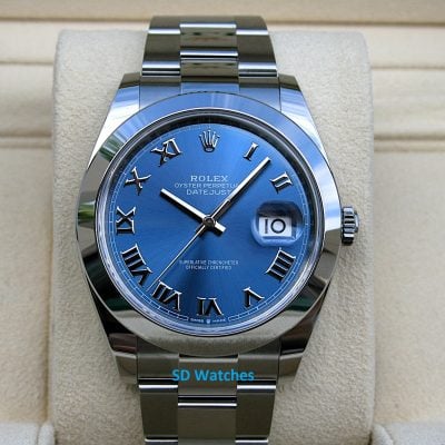 Blue Rolex Datejust wristwatch with Roman numerals and date window on a beige display pillow. (informative)