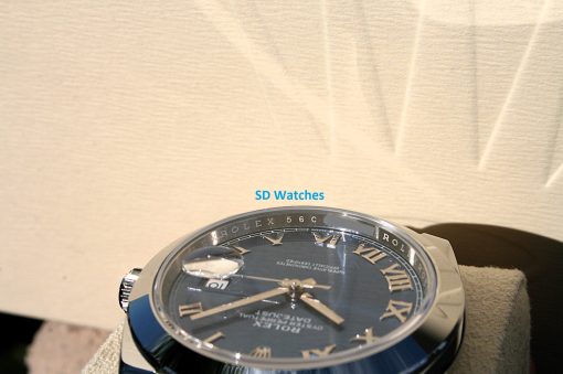 IMG_6701 | SD Watches Close-up of a Rolex-style wristwatch with Roman numerals on a beige background; blue 'SD Watches' text above the dial.