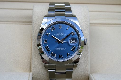 IMG_6707 | SD Watches Close-up of a silver Rolex wristwatch with a blue dial, Roman numeral hour markers, and a date window at 3 o'clock on a beige display cushion.