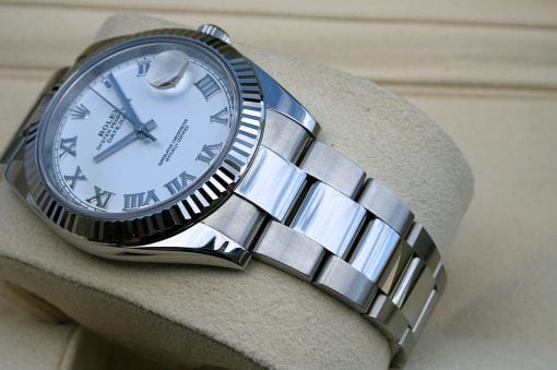 IMG_6713 | SD Watches Close-up of a silver Rolex Datejust wristwatch with Roman numerals on a white dial, fluted bezel, and date magnifier on a beige cushion.