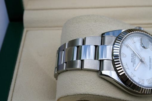 IMG_6714 | SD Watches Close-up of a stainless steel Rolex bracelet and fluted bezel resting on a beige cushion, showing part of a white dial and Roman numerals.