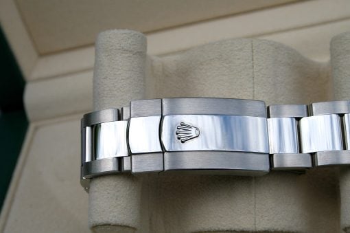 IMG_6715 | SD Watches Close-up of a stainless steel Rolex bracelet clasp with the iconic crown logo, mounted against a beige background.