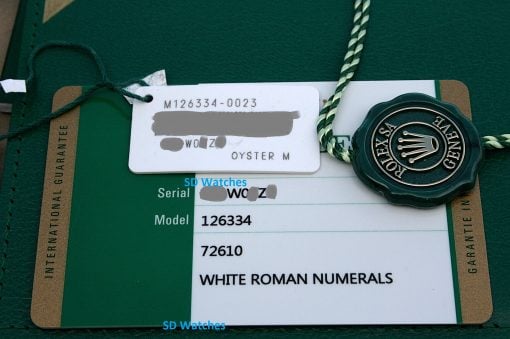 IMG_6720 | SD Watches Close-up of a Rolex tag on a green warranty card: a white tag with a serial/model number and a green circular Rolex seal, attached by a braided string.