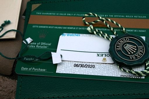 IMG_6721 | SD Watches Close-up of a Rolex warranty card with a green tag and braided cords, and the blue text 'SD Watches' overlaying the image.