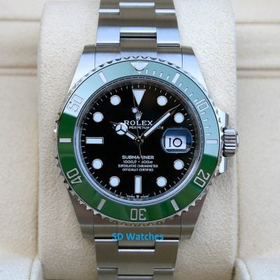 Rolex Submariner stainless steel watch with black dial and green bezel resting on a beige cushion, showing the date at 3 o'clock with a magnifier.