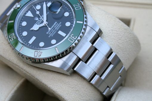 IMG_6778 | SD Watches Close-up of a stainless steel Rolex Submariner watch with a green bezel resting on a beige cushion.