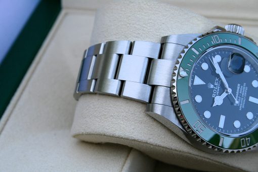 IMG_6779 | SD Watches Close-up of a stainless steel Rolex watch with a green bezel resting on a beige cushion/cushioned display surface.