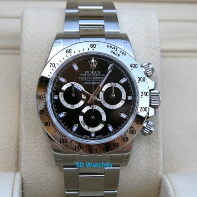 Close-up of a stainless steel Rolex Daytona watch with black dial and tachymeter bezel on a beige display cushion.
