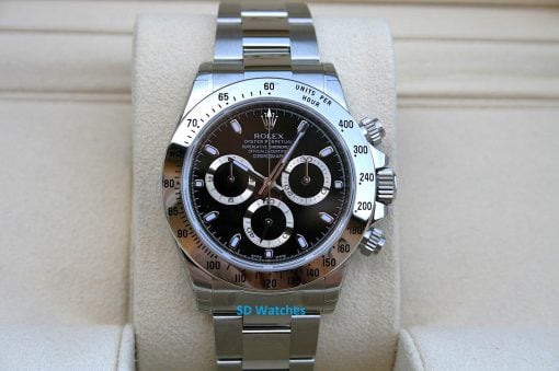 Rolex 116520 NOS | SD Watches Close-up of a stainless steel Rolex Daytona watch with black dial and tachymeter bezel on a beige display cushion.