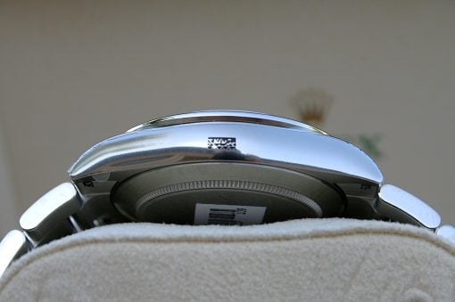 IMG_6825 | SD Watches Close-up of a shiny chrome object with a barcode label resting on beige fabric.