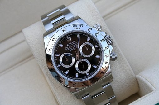 IMG_6836 | SD Watches Close-up of a stainless steel Rolex Daytona watch with a black dial and tachymeter bezel on a beige cushion.