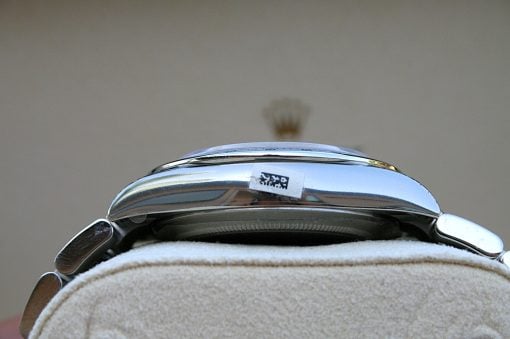 IMG_6848 | SD Watches Close-up of a polished chrome dome resting on a soft beige surface, with a small label or sticker visible on its side.