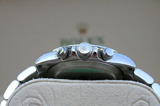 IMG_6849 | SD Watches Close-up of a polished silver Rolex crown on a metal watch case, resting on a soft beige surface