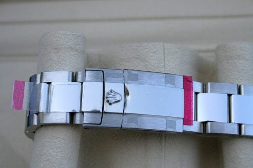 IMG_6850 | SD Watches Close-up of a silver stainless steel watch band wrapped around a beige pillar, with pink tape at the ends and the Rolex crown logo visible on the clasp.