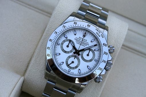 IMG_6863 | SD Watches Close-up of a silver Rolex Daytona watch on a beige cushion, showing chronograph subdials and tachymeter bezel