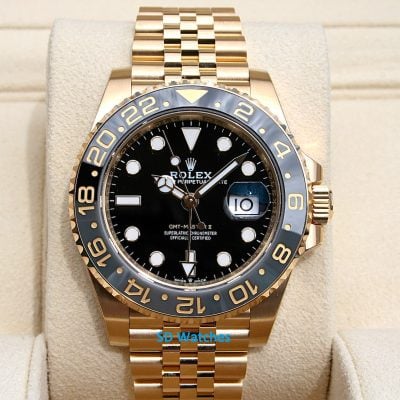 Gold Rolex GMT-Master II wristwatch with black dial on beige display cushion, gold bezel and bracelet