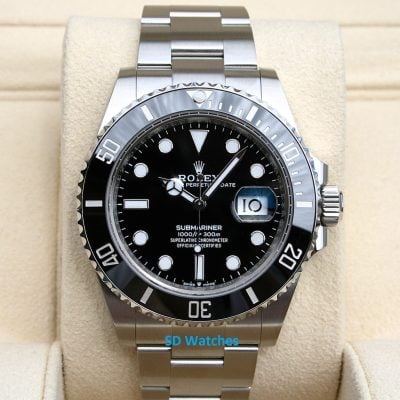 Close-up of a stainless steel Rolex Submariner watch with black dial on a beige display cushion, showing date magnifier.