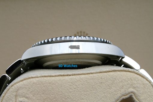IMG_6913 | SD Watches Close-up of a silver wristwatch resting on a beige fabric surface, with a textured bezel and a blue 'SD Watches' logo visible beneath the case.