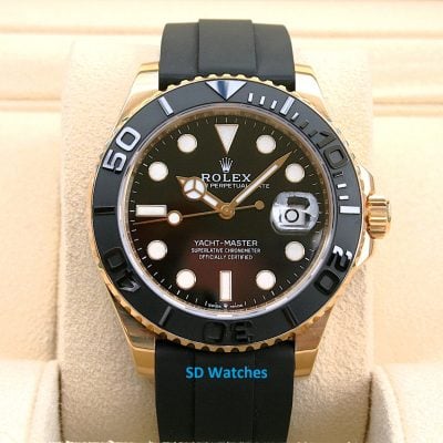 Rolex Yacht-Master watch with a black dial, gold bezel and black rubber strap on a beige display cushion.