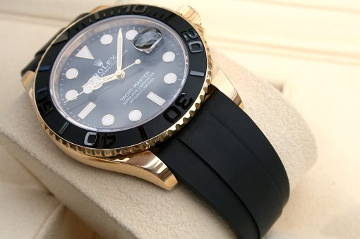 IMG_6930 | SD Watches Gold Rolex Yacht-Master watch with black ceramic bezel, gold case, and black rubber strap resting on a beige surface