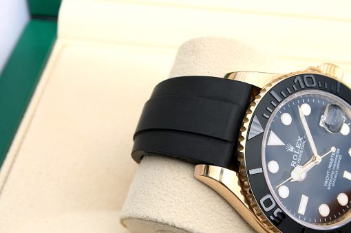 IMG_6931 | SD Watches Close-up of a gold Rolex watch with a black rubber strap resting on a beige display cushion, showing a black bezel and detailed dial.