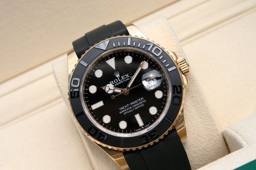 IMG_6940 | SD Watches Gold Rolex Yacht-Master watch with a black dial, fluted bezel, and black rubber strap resting on a beige cushion.