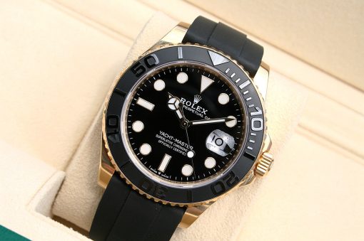 IMG_6943 | SD Watches Rolex Yacht-Master watch with black dial, gold bezel, and black rubber strap displayed on a beige cushion, angled for a close look