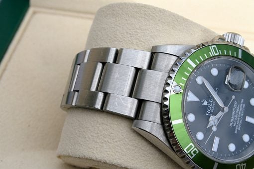 IMG_6948 | SD Watches Close-up of a stainless steel Rolex Submariner watch with a green bezel resting on a beige surface.
