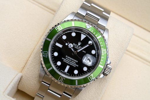 IMG_6957 | SD Watches Close-up of a stainless steel Rolex Submariner watch with a green bezel on a beige cushion surface, showing a black dial and date window.