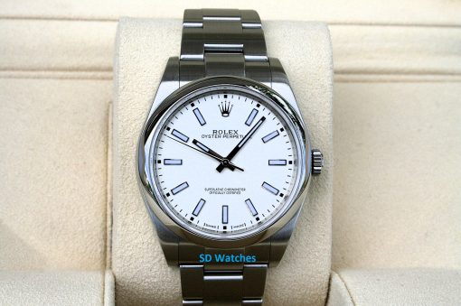 Rolex 114300 | SD Watches Rolex Oyster Perpetual wristwatch with a white dial and stainless steel bracelet displayed on a beige cushion.