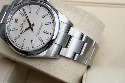 IMG_6966 | SD Watches Close-up of a silver Rolex Oyster Perpetual wristwatch with a white dial and metal bracelet on a beige cushion surface.