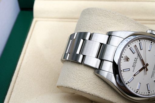 IMG_6967 | SD Watches Close-up of a stainless steel Rolex Oyster Perpetual wristwatch resting on a beige cushion inside a green presentation box, showing its white dial and brushed bracelet links.