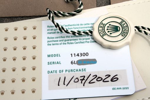 IMG_6976 | SD Watches Close-up of a Rolex seal tag and purchase form, showing model 114300 and green text on the card with a green/white braided string nearby.
