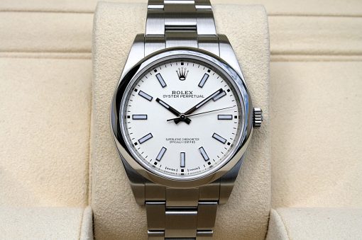 IMG_6982 | SD Watches Close-up of a stainless steel Rolex Oyster Perpetual wristwatch with a white dial, silver baton hour markers, and the crown logo, resting on a beige display cushion.