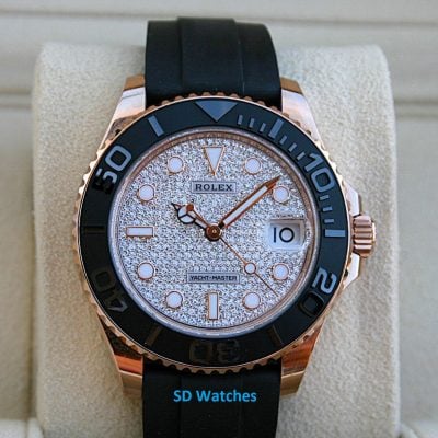 Rose gold Rolex Yacht-Master watch with a diamond-paved dial, black bezel, and black strap displayed on a beige cushion.
