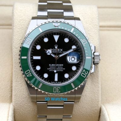Rolex Submariner watch with black dial and green bezel on a beige display cushion.