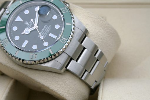 IMG_7073 | SD Watches Close-up of a stainless steel Rolex Submariner watch with a green bezel resting on a beige fabric surface.