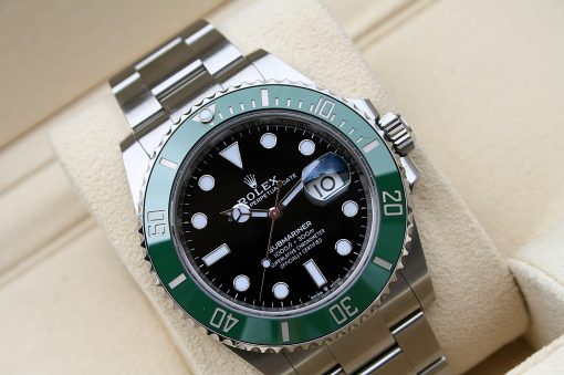 IMG_7083 | SD Watches Close-up of a Rolex Submariner watch with a green bezel, black dial, and stainless steel bracelet on a beige surface.