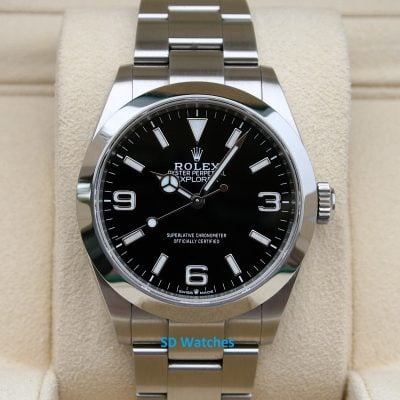 Close-up of a stainless steel Rolex Oyster Perpetual Explorer watch with a black dial, silver hour markers, and bracelet on a beige display cushion.