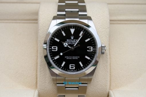 Rolex 224270 | SD Watches Close-up of a stainless steel Rolex Oyster Perpetual Explorer watch with a black dial, silver hour markers, and bracelet on a beige display cushion.