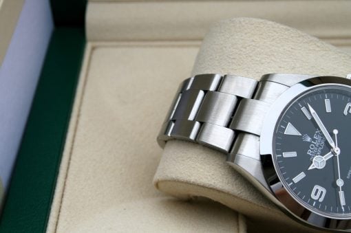 IMG_7091 | SD Watches Close-up of a stainless steel Rolex wristwatch with a dark dial and silver bracelet resting on a beige display cushion in a box.