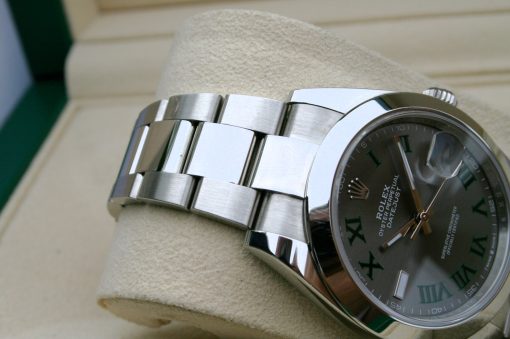 IMG_7125 | SD Watches Close-up of a stainless steel Rolex watch resting on a beige cushion, showing a dark dial with green Roman numerals and brushed bracelet links.