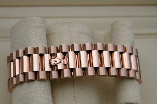 IMG_7146 | SD Watches Close-up of a copper-toned segmented bracelet with a small crown emblem on a soft grey display cushion.